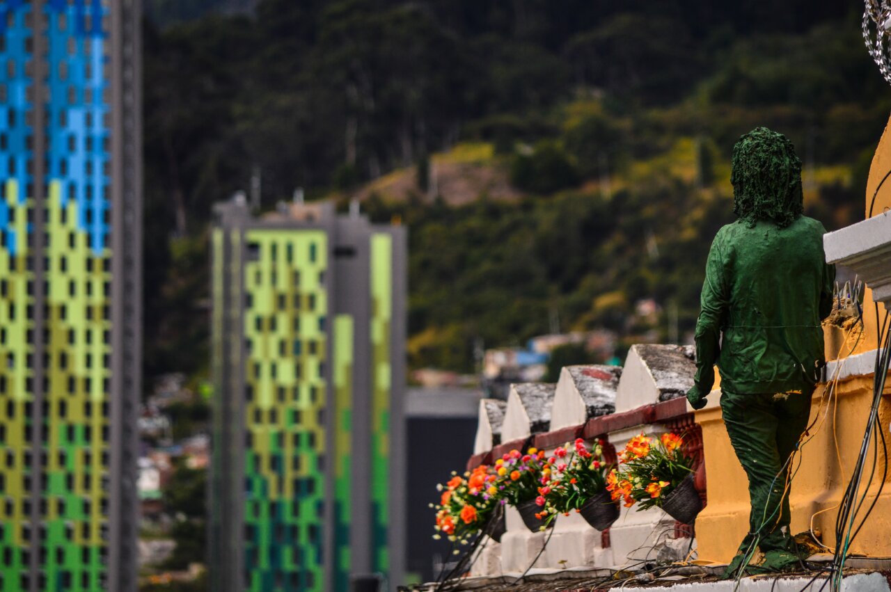 Vista de una figura verde en un balcón con edificios coloridos al fondo