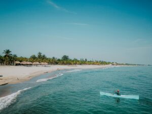 Vista de un hombre en kayak en la playa de Tela con palmeras al fondo