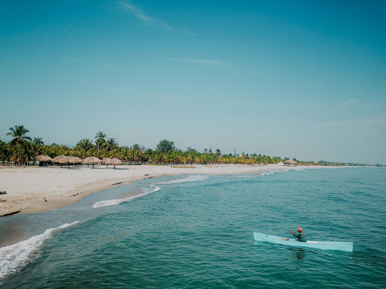 Vista de un hombre en kayak en la playa de Tela con palmeras al fondo
