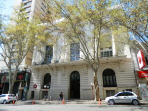 Edificio de la Dirección de Turismo en Mendoza con árboles y vehículos