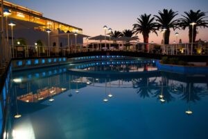 Vista nocturna de un hotel con piscina iluminada y palmeras