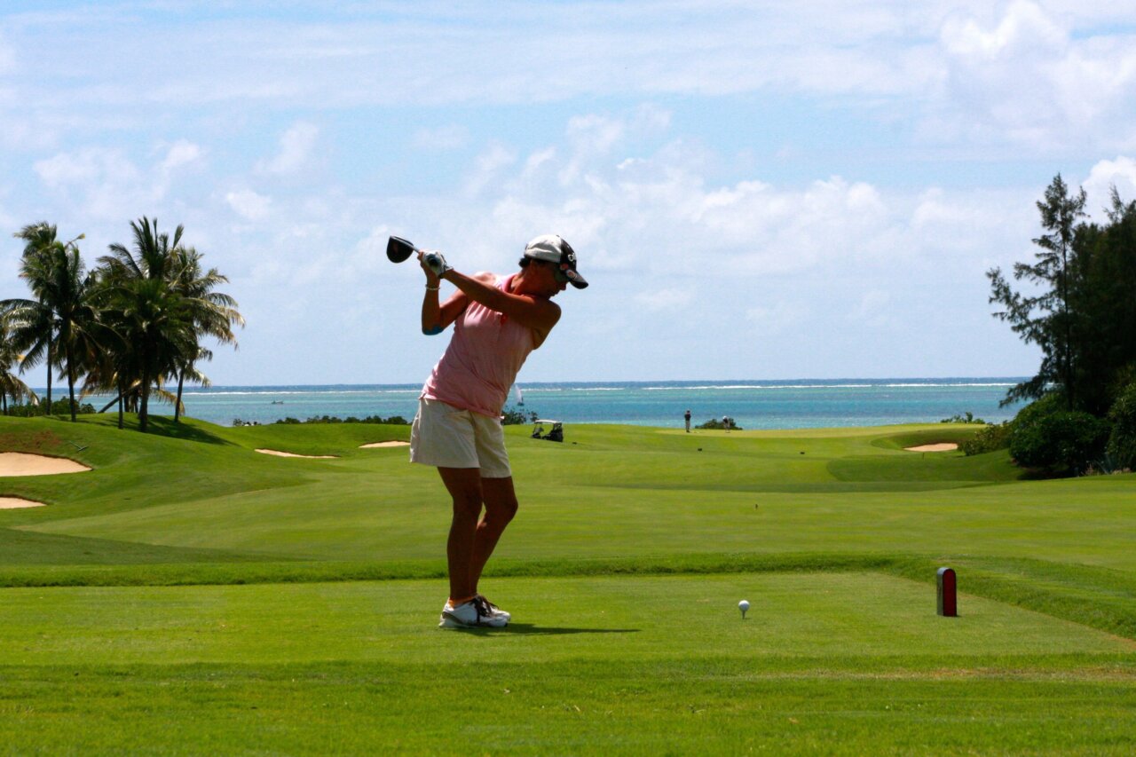 Mujer jugando golf en un campo con vista al mar