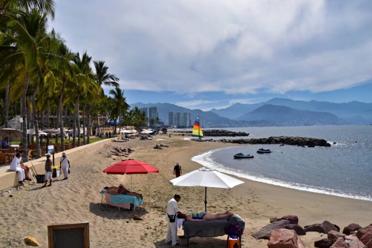 Vista de una playa con palmeras y montañas al fondo
