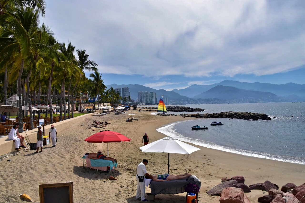 Vista de una playa con palmeras y montañas al fondo