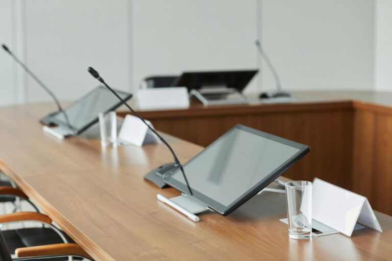 Mesa de conferencias con micrófonos y pantallas táctiles en un entorno moderno.