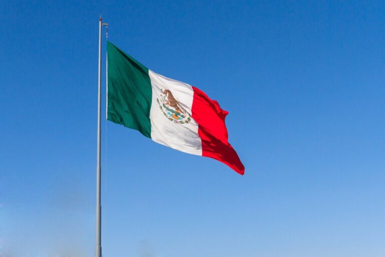 Bandera de México ondeando bajo un cielo azul claro