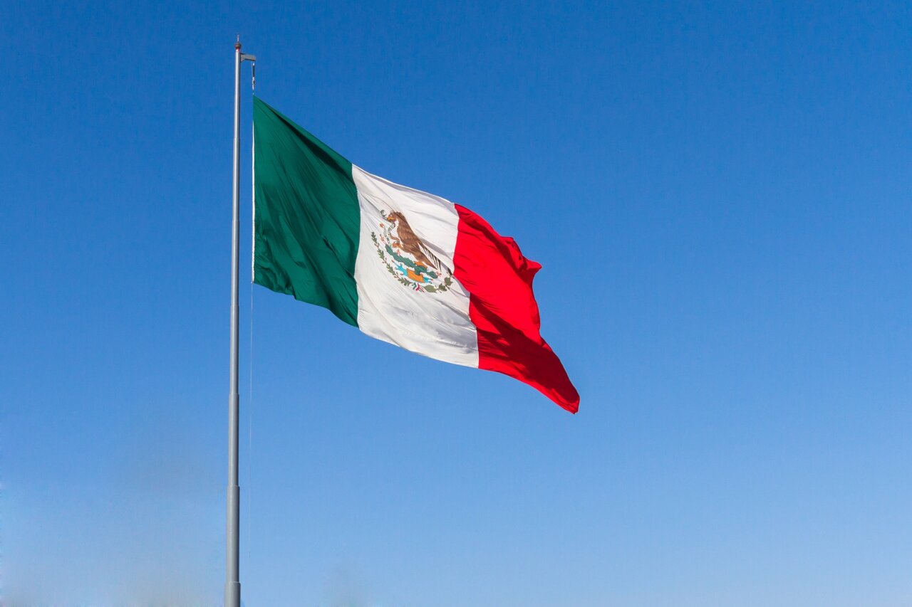 Bandera de México ondeando bajo un cielo azul claro