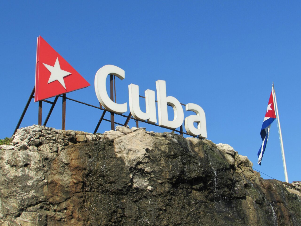 Cartel que dice Cuba con bandera cubana al fondo