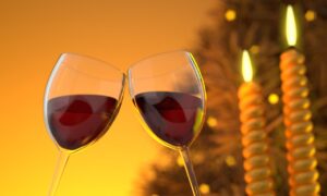 Dos copas de vino tinto brindando con fondo cálido y velas encendidas.