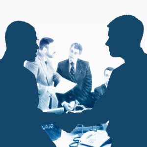 Dos personas estrechando manos en un entorno de oficina con otros hombres de fondo.